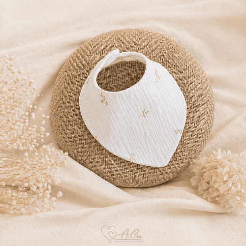 Bavoir bébé collection Rosée d’éveil en double gaze fleurie posé sur rond en rotin ambiance naturelle
